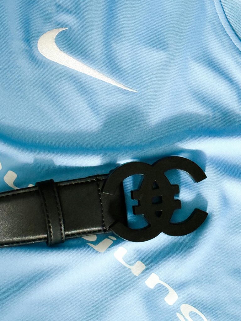 Close-up of a luxurious black leather belt with unique buckle on a blue fabric background.