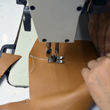 Close-up view of sewing machine stitching leather fabric, focusing on industrial crafting process.