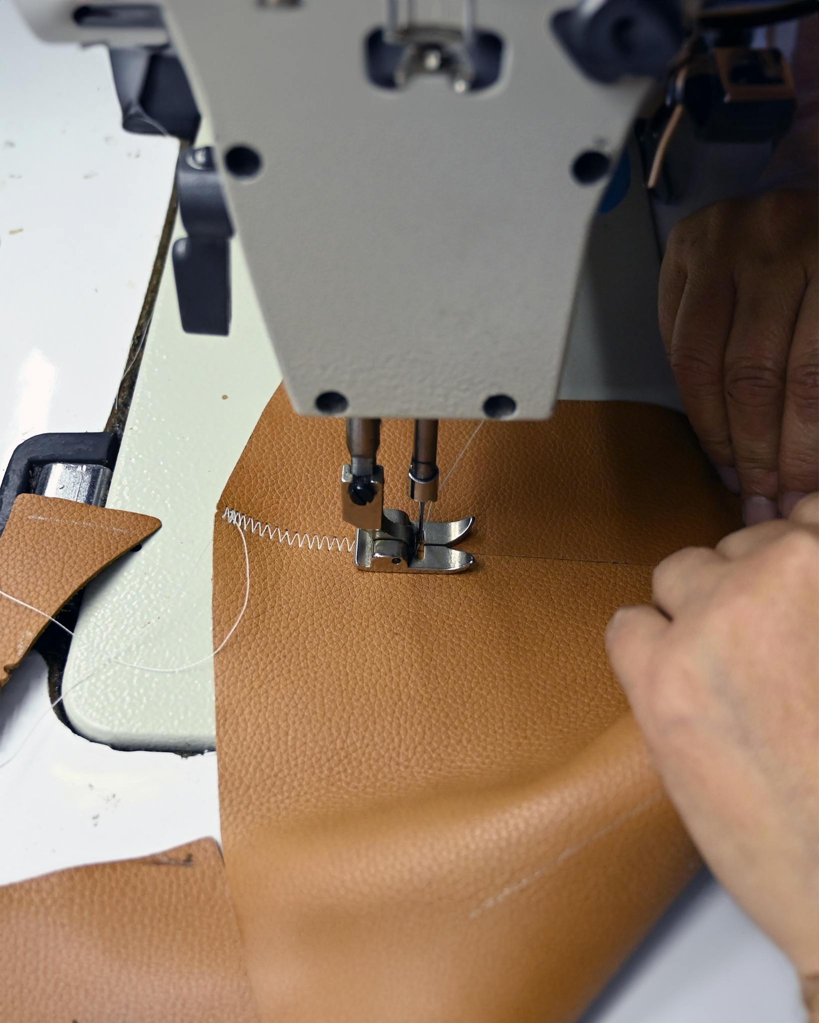 Close-up view of sewing machine stitching leather fabric, focusing on industrial crafting process.