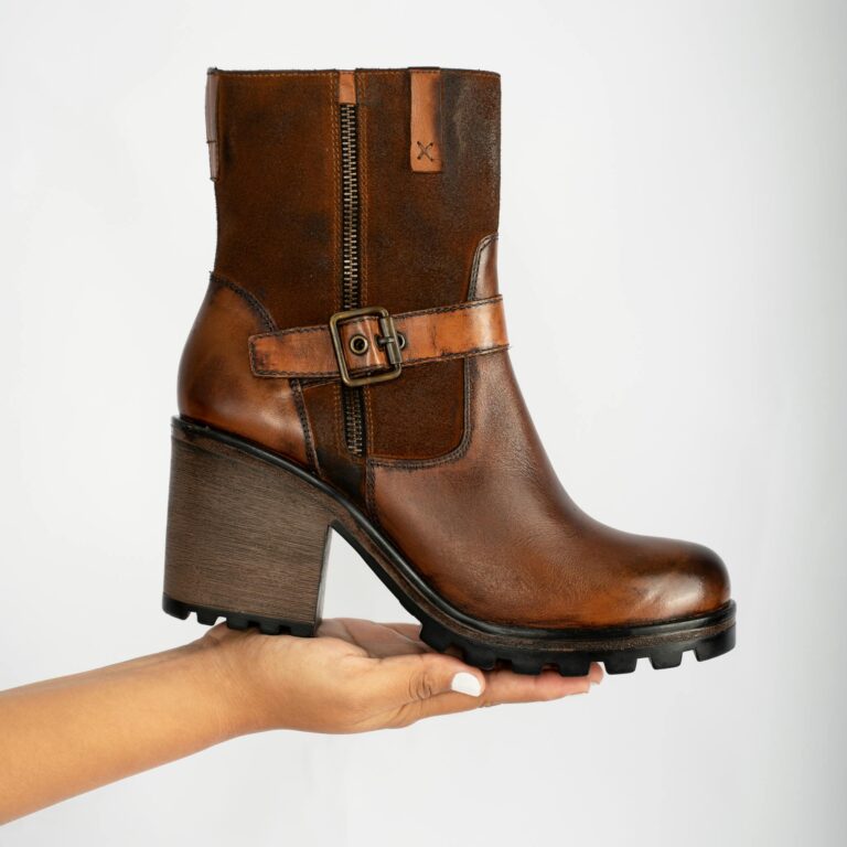 Elegant brown leather ankle boot with block heel and buckle detail, showcased on a hand.